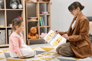 Autism therapy. Little girl choosing emoticon with teacher in ABA therapy center